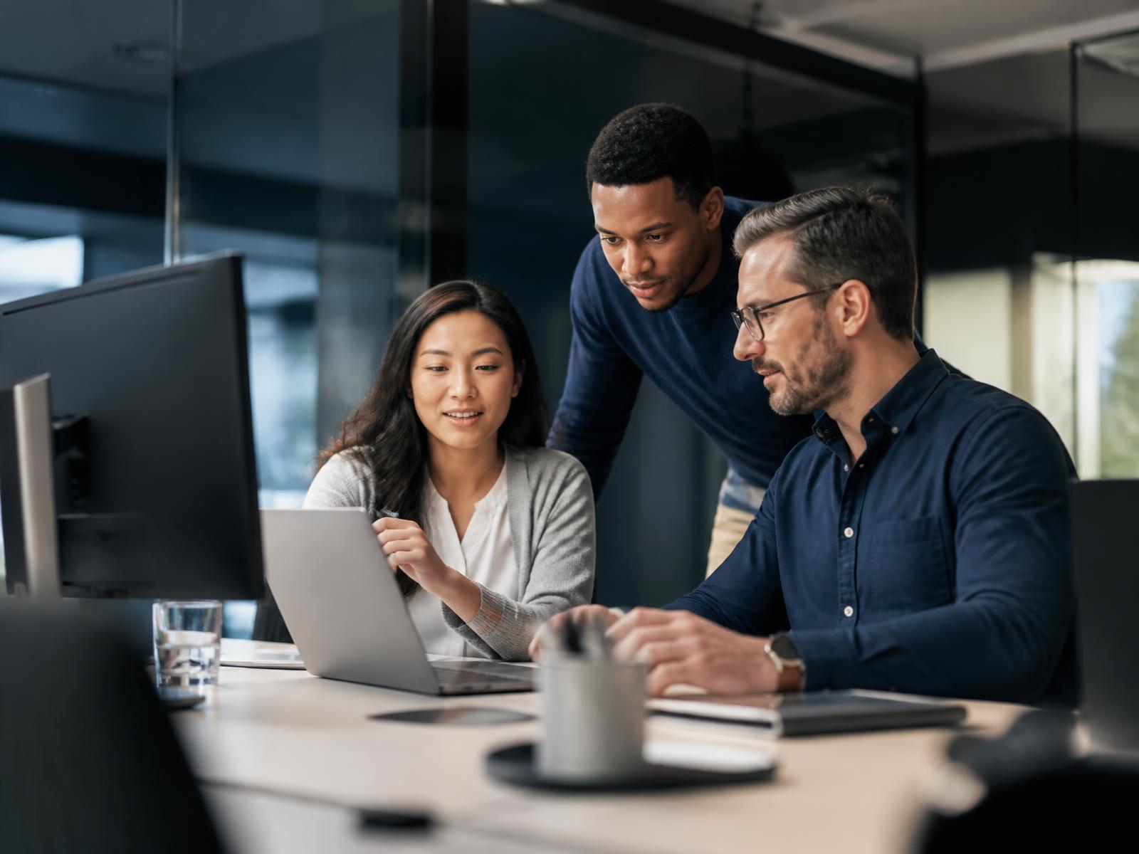 Three professional colleagues reviewing work together at a modern office workstation